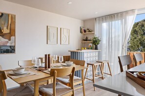 Un espace repas avec une table et des chaises en bois, un coin cuisine avec un bar, et une vue sur la verdure à l’extérieur.