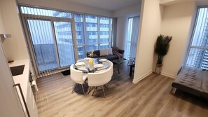 Een modern appartement met een eethoek, een bank, een groot raam en een balkon.