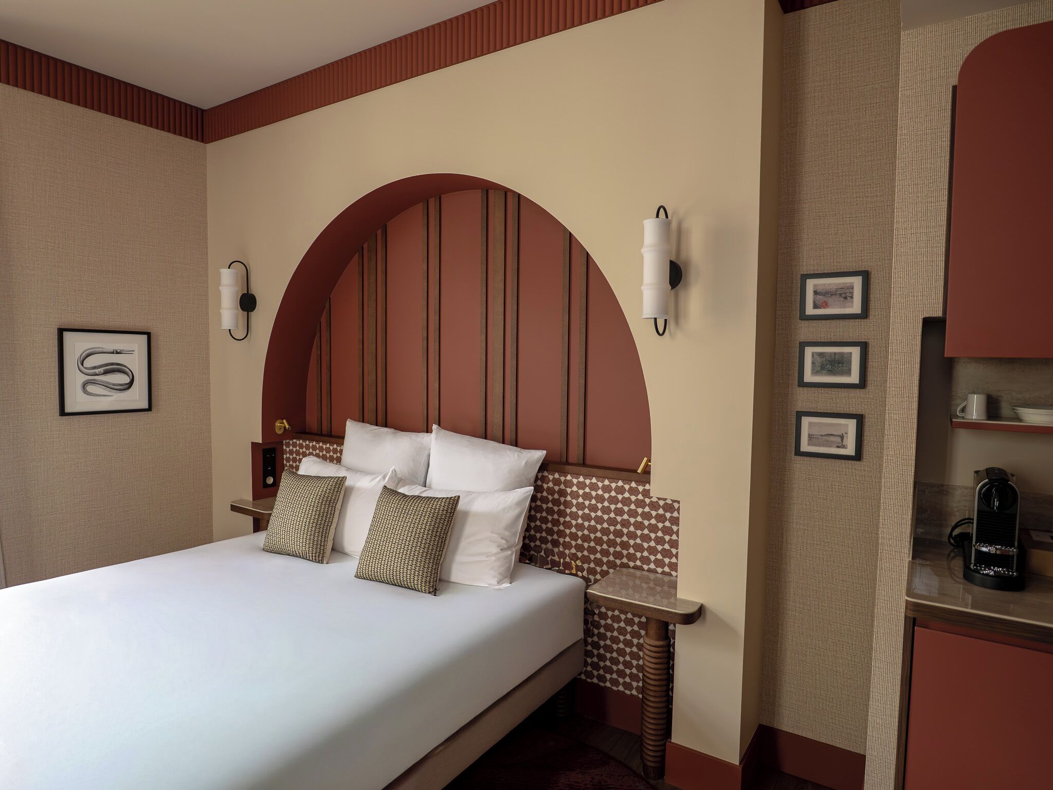 Habitación de hotel con una cama grande, dos mesitas de noche, una lámpara de pared y una repisa con cuadros enmarcados.