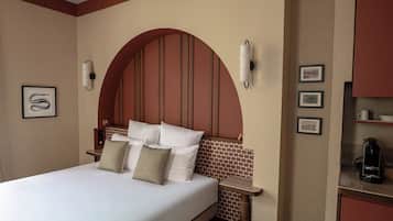 Habitación de hotel con una cama grande, dos mesitas de noche, una lámpara de pared y una repisa con cuadros enmarcados.