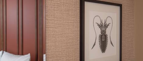 Una obra de arte en marco que muestra un escarabajo sobre una pared con textura en una habitación de hotel.