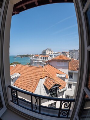 Vista desde una ventana con balcón, con vistas a una zona costera con edificios y un faro.