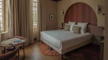 Ein Hotelzimmer mit einem großen Bett, einem kleinen Tisch mit Stuhl und einem Fenster mit Vorhängen.