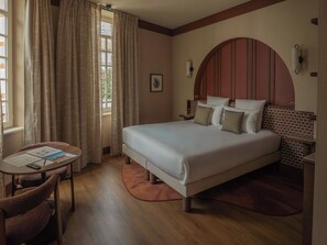 A hotel room with a large bed, a small table with a chair, and a window with curtains. - Maison Atalaye - Hôtel entièrement rénové (Biarritz)