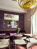 Un comedor con mesas redondas, sillas de mimbre, un espejo en la pared y una lámpara decorativa en el techo.