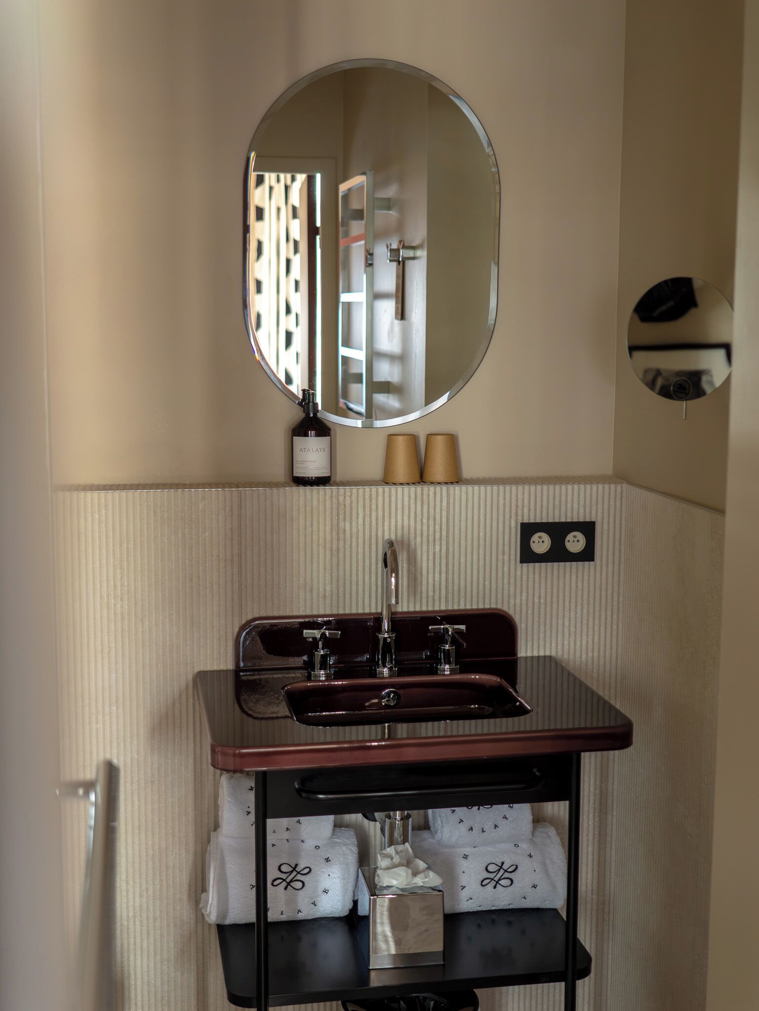 A bathroom with a round mirror, a sink with a faucet, and a towel rack with folded towels.