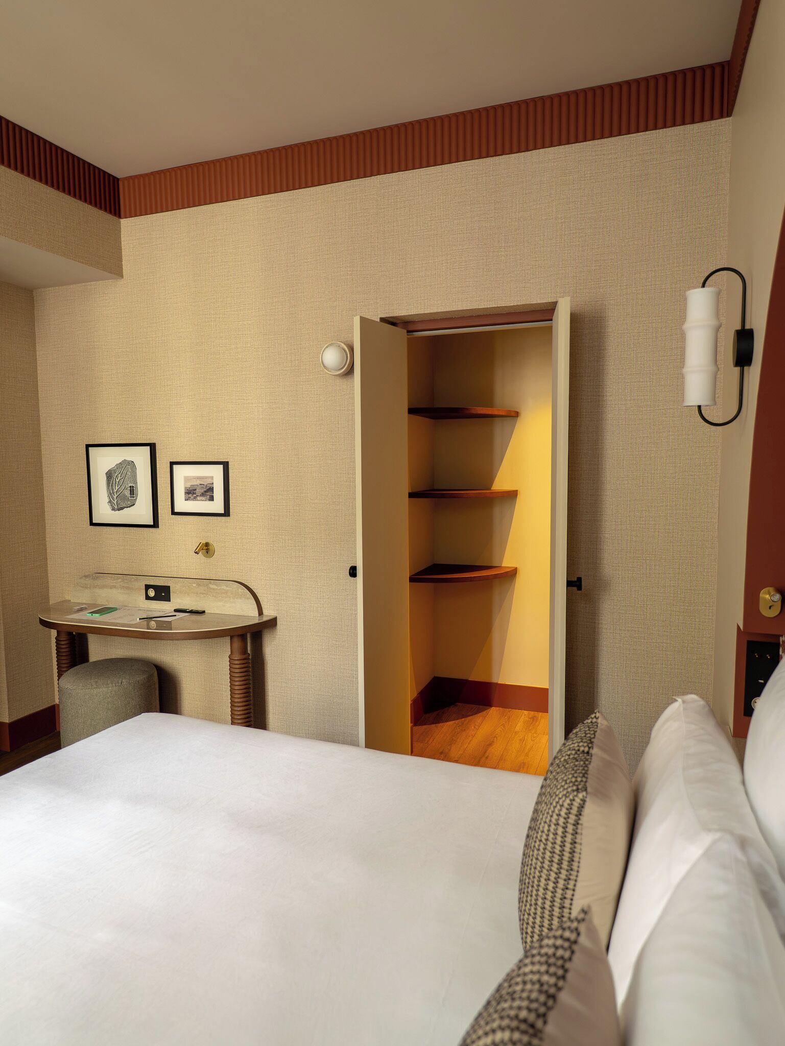 Une chambre d’hôtel comprenant un lit, un bureau avec une chaise, une armoire et deux tableaux encadrés accrochés au mur.
