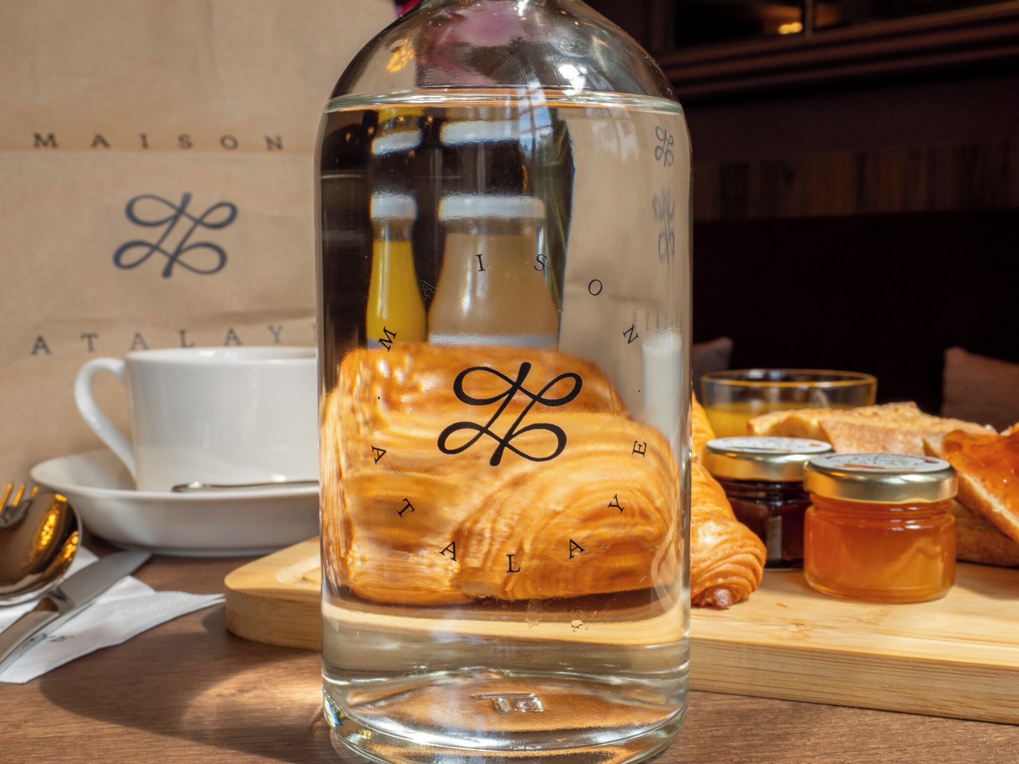 Een glazen fles met een gebakje, een witte kop en schotel, en een houten plank met gebak en potten.