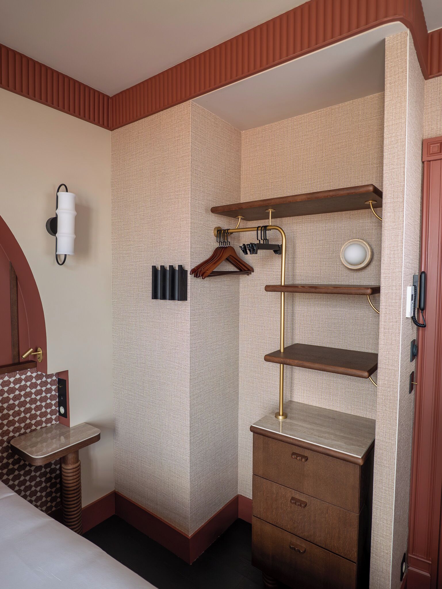 Una habitación de hotel compacta con cama, un escritorio pequeño, un armario y un estante en la pared.