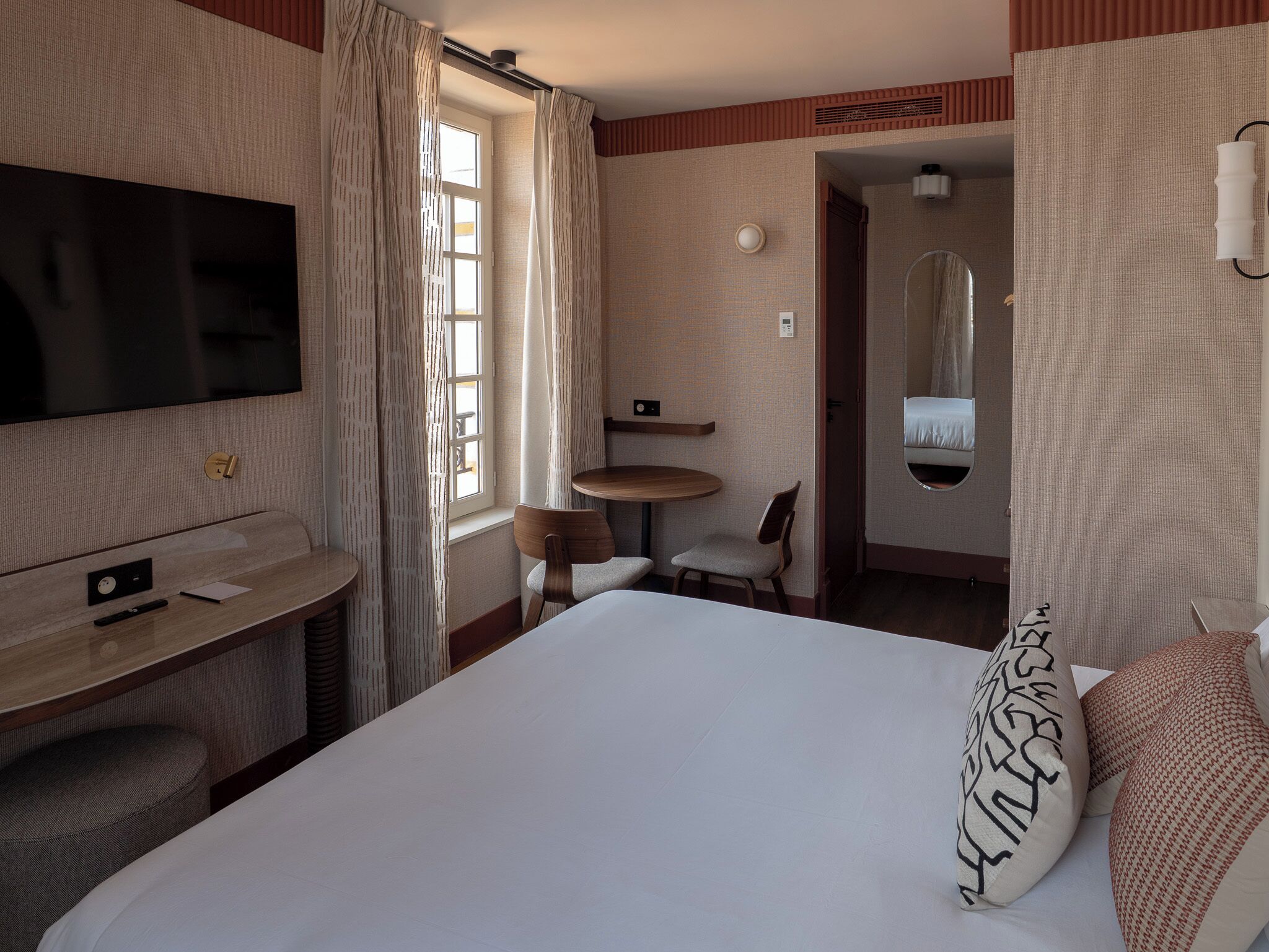 Une chambre d’hôtel équipée d’un lit, d’un bureau, d’une chaise, d’une télévision et d’une salle de bain avec un miroir.