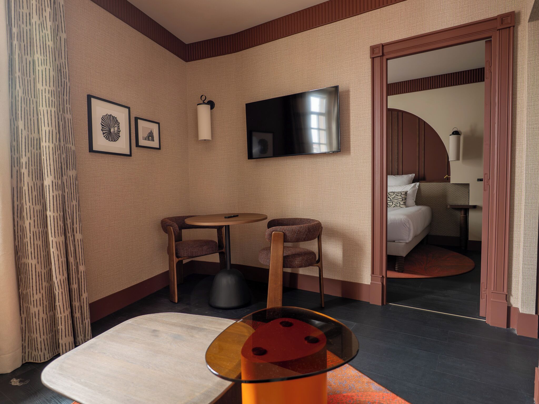 Une chambre d’hôtel avec un lit, une télévision, une petite table avec des chaises et une fenêtre avec des rideaux.
