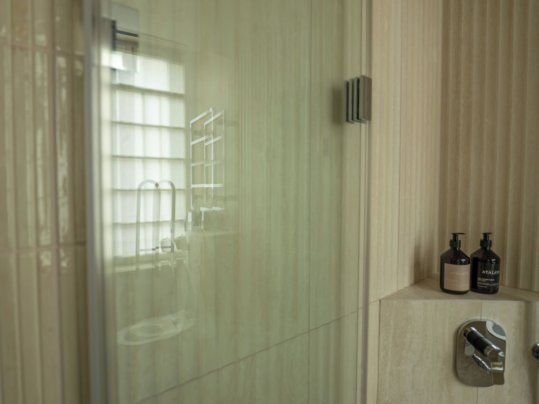Un bagno con box doccia in vetro, un portascopino e due flaconi di lozione su un mobile lavabo.