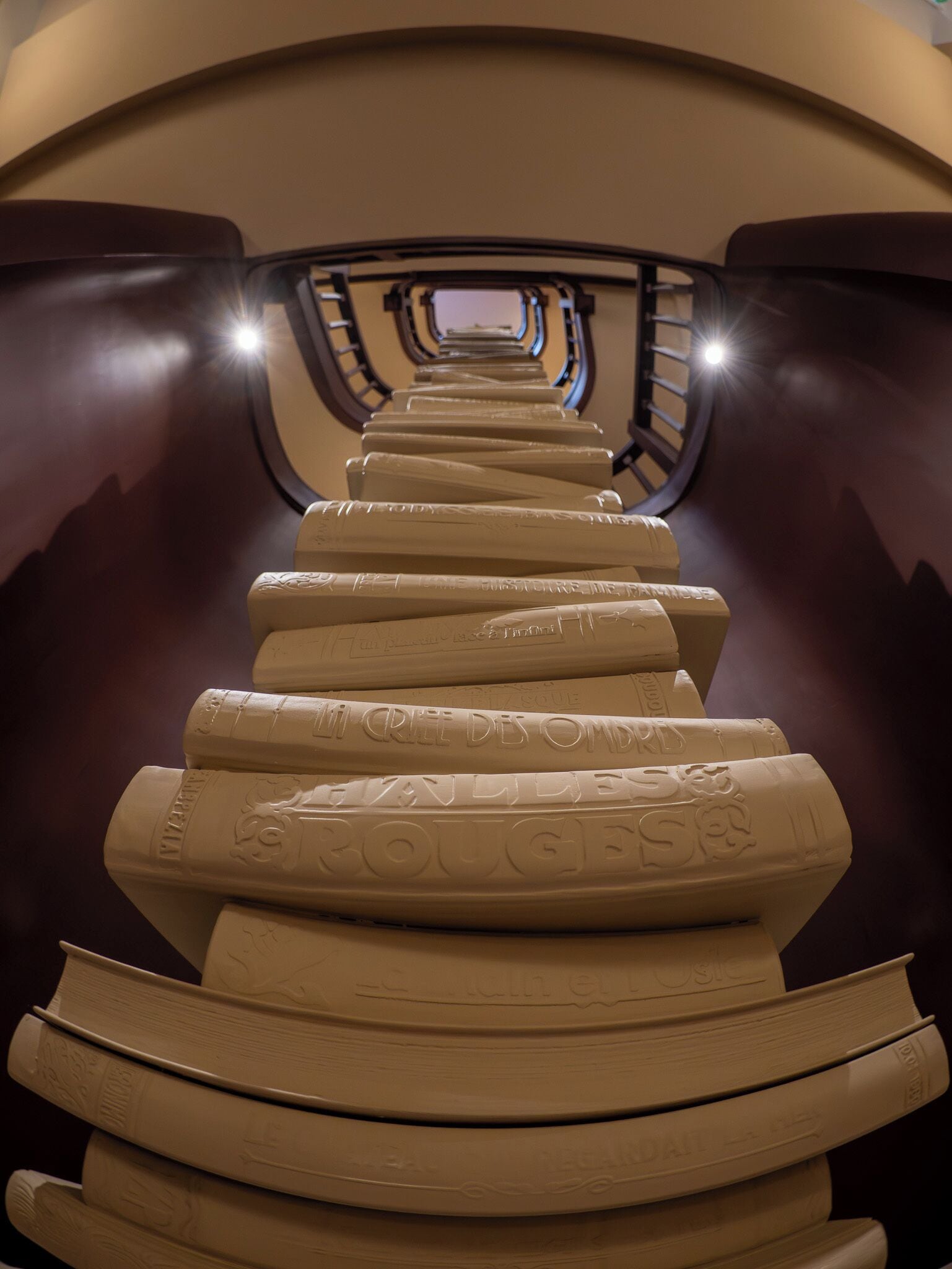 A spiral staircase with engraved steps leading upwards, surrounded by dark walls and a curved ceiling.