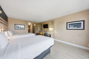 Une chambre d’hôtel avec un grand lit, un bureau, une chaise, une télévision et deux tableaux encadrés au mur.