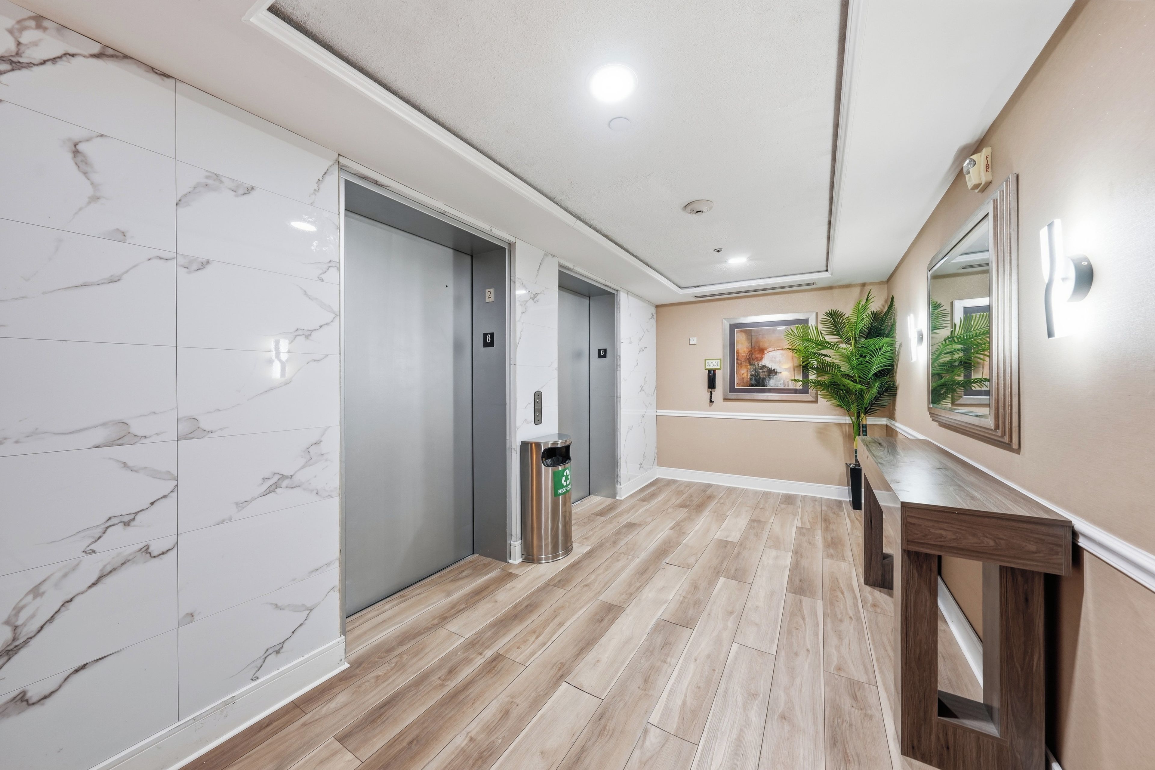 A hallway with marble flooring, two elevators, a recycling bin, and a wooden bench.