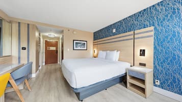 Hotellihuone, jossa on sänky, yöpöytä, työpöytä, tuoli ja sinisellä kuviolla koristeltu seinä.