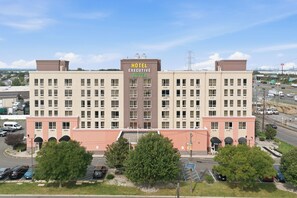 Un hôtel à plusieurs étages, avec une enseigne bien visible indiquant « Hotel Executive Suites », et un parking situé devant l’entrée.