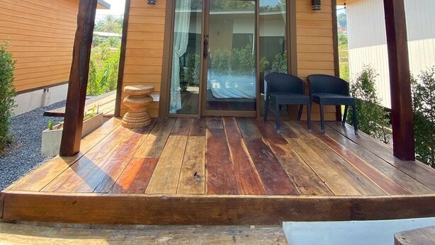 Eine Holzterrasse mit überdachtem Patio und einer Glastür sowie zwei Stühlen.