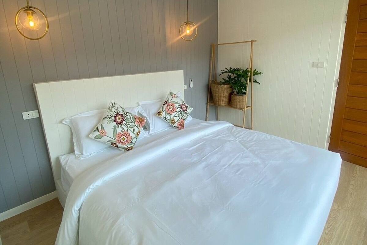 A bedroom with a bed, two pendant lights, a bedside plant, and a wooden door.