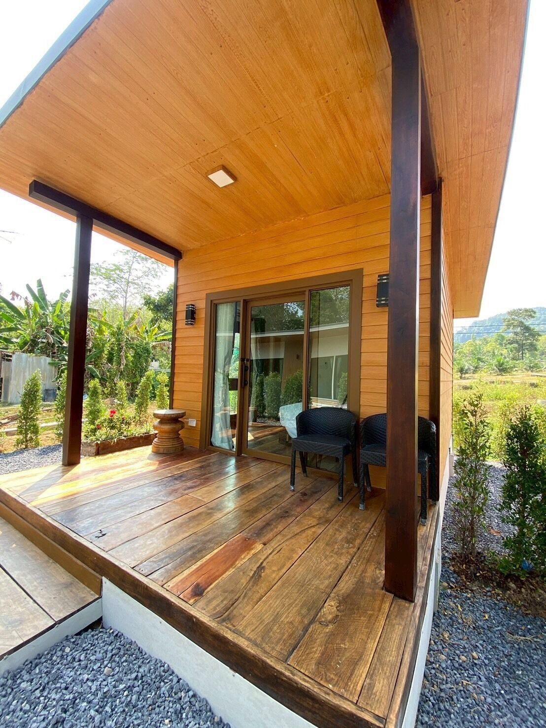Una terraza de madera con un ventanal de vidrio que da a un patio, rodeado de follaje.
