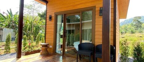 Una terraza de madera con un ventanal de vidrio que da a un patio, rodeado de follaje.