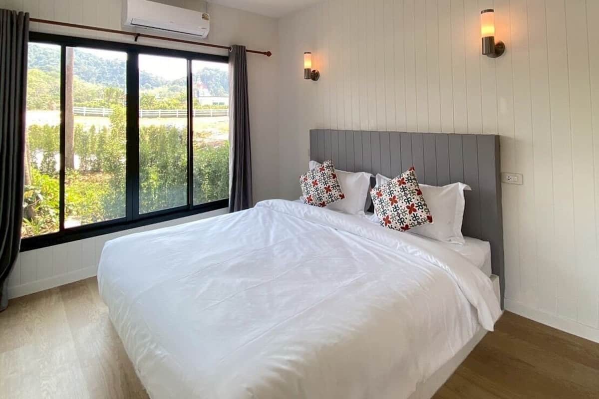 A bedroom with a large bed, two wall-mounted lights, an air conditioning unit, and a window with curtains.