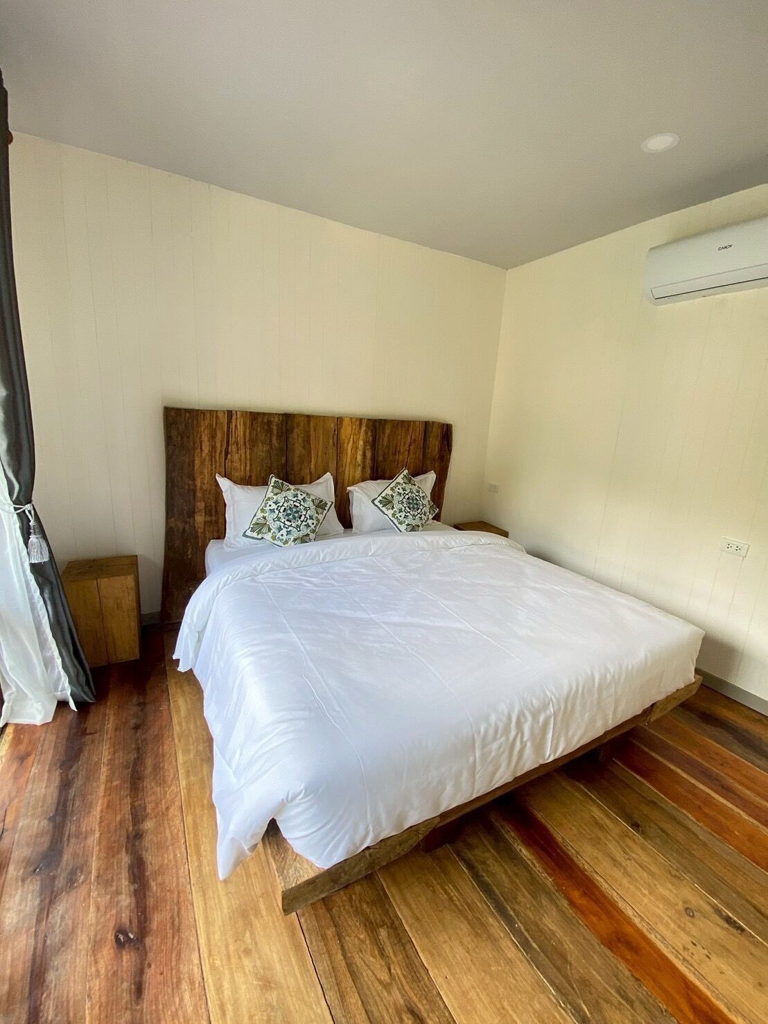 A bedroom with a wooden headboard, a large bed with white bedding, a wooden nightstand, and a small bedside table.