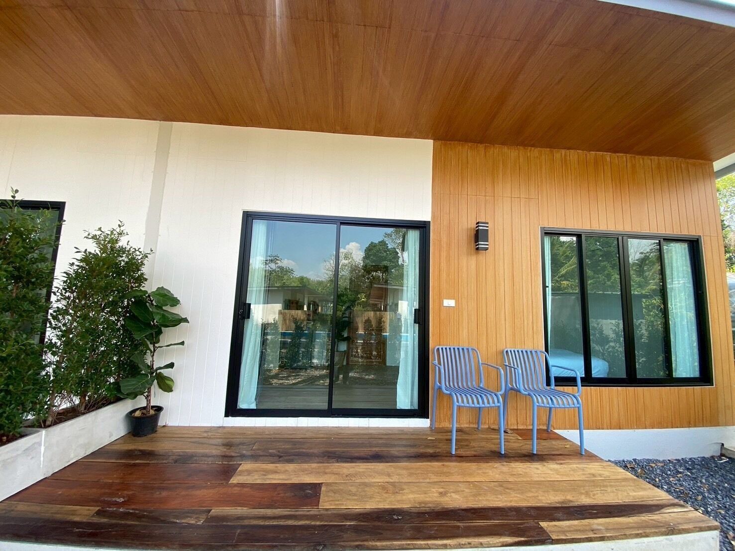 A modern building with a wooden ceiling, large sliding glass doors, and two metal chairs on a wooden deck.