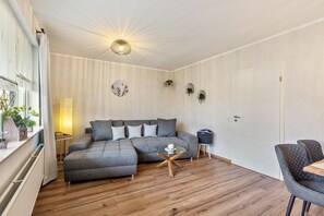 A modern living room with a sectional sofa, a small round coffee table, and a dining area with a table and chairs. - Apartment Magnolie – with MeineCardPlus and New Furnishings for 4 Guests (Willingen (Upland))