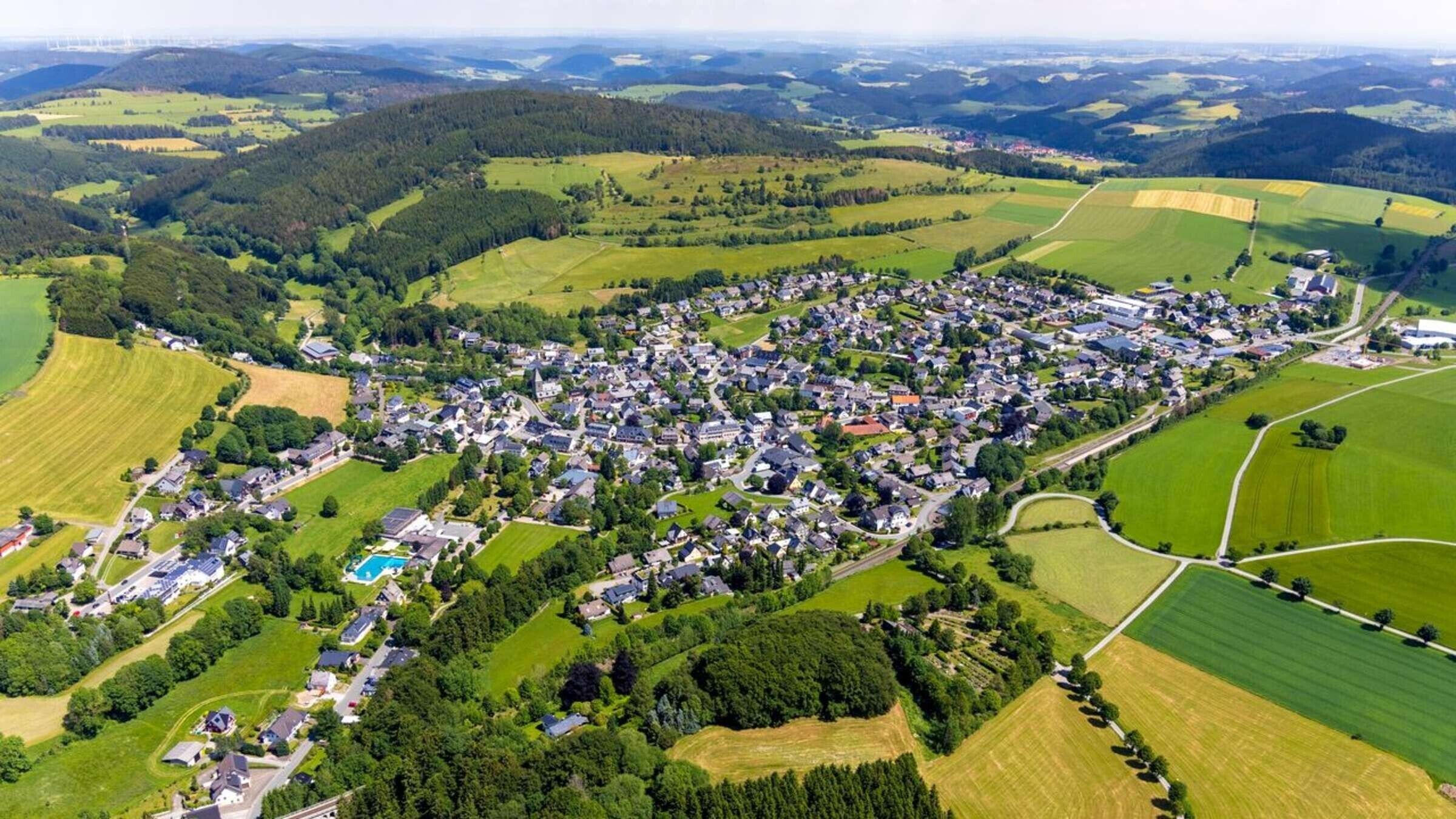 Vista aérea de un pueblo rural con casas, campos y una piscina.