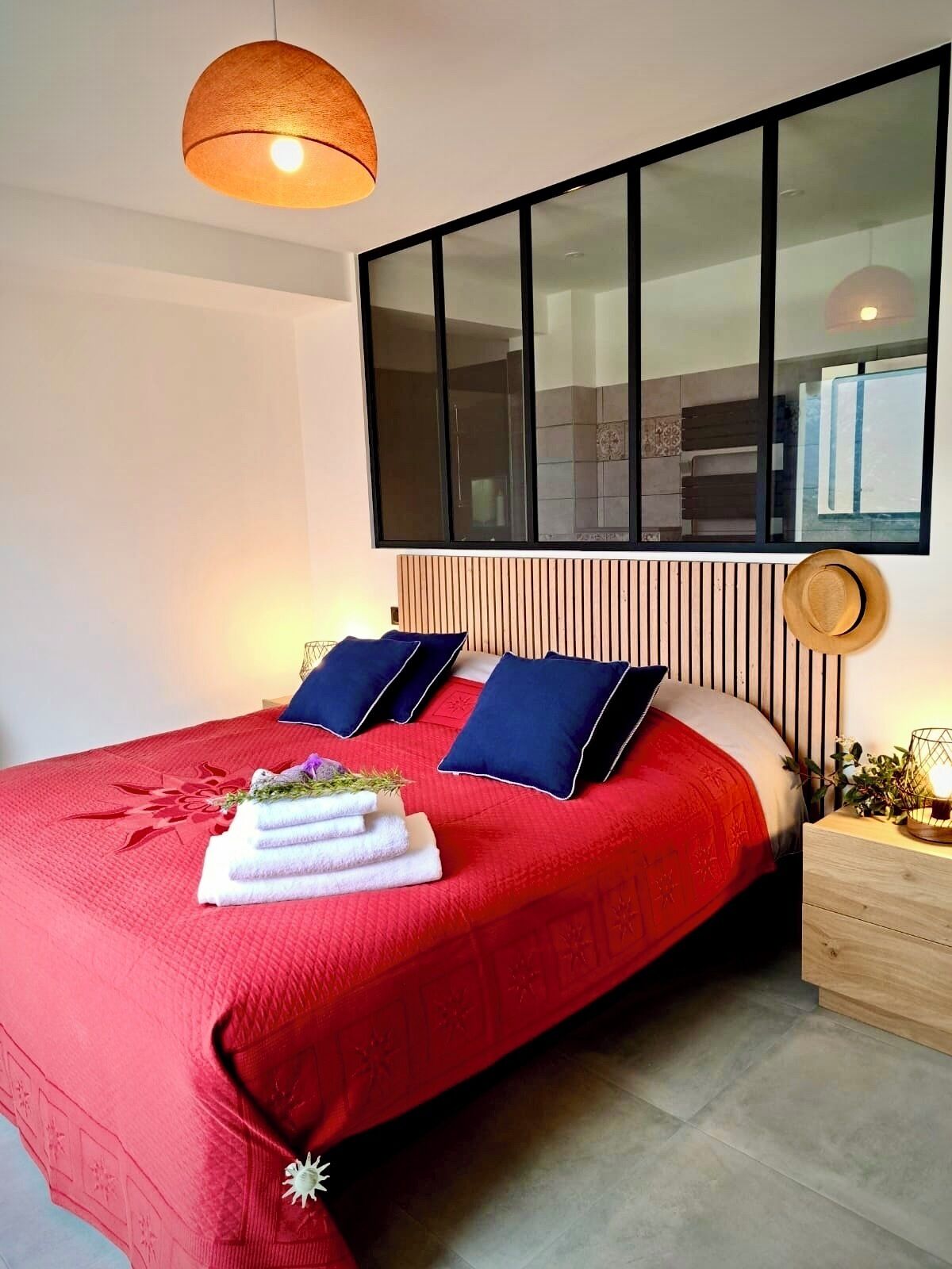A modern bedroom with a large bed, a wooden headboard, a large window, and a bedside table with a lamp.
