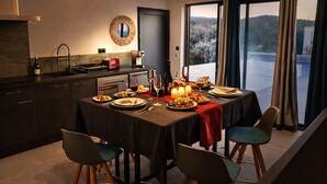Un comedor con una mesa dispuesta para cuatro personas, una cocina con armarios oscuros, un tostador rojo y vistas a un paisaje montañoso a través de grandes ventanales.