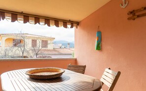 A balcony with a table, chairs, a woven basket, and a view of buildings. - Villaggio degli Ulivi (San Teodoro)