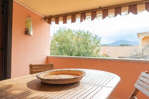 A balcony with a table, chairs, a woven basket, and a view of greenery and mountains. - Villaggio degli Ulivi (San Teodoro)