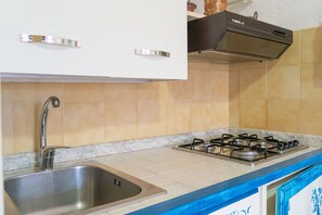 Een keuken met een roestvrijstalen spoelbak, een gasfornuis, witte kastjes en een betegelde spatwand.