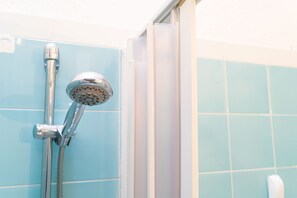 A shower with a handheld showerhead and a hose, a tiled wall, and a partially visible door. - Villaggio degli Ulivi (San Teodoro)