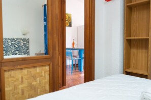A bedroom with a wooden headboard, a bed, a wooden wardrobe, and a view into a dining area with a table and chairs. - Villaggio degli Ulivi (San Teodoro)