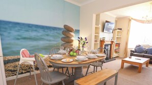 Un coin repas avec une table ronde dressée pour quatre personnes, un banc en bois et une vue sur l’océan.