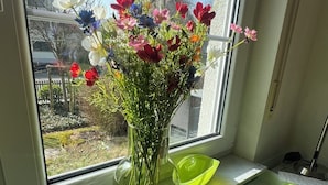 Un vase en verre transparent contenant un bouquet de fleurs, posé sur un rebord de fenêtre.