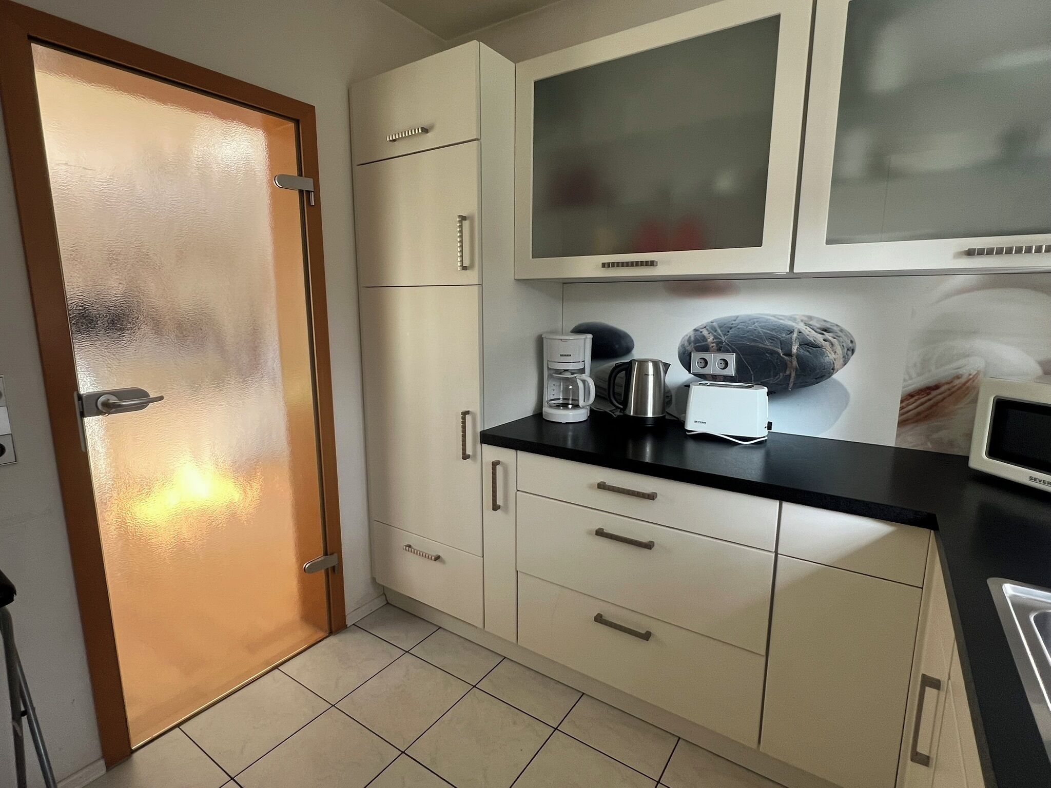 A kitchen with white cabinets, a black countertop, a coffee maker, a toaster, and a microwave.
