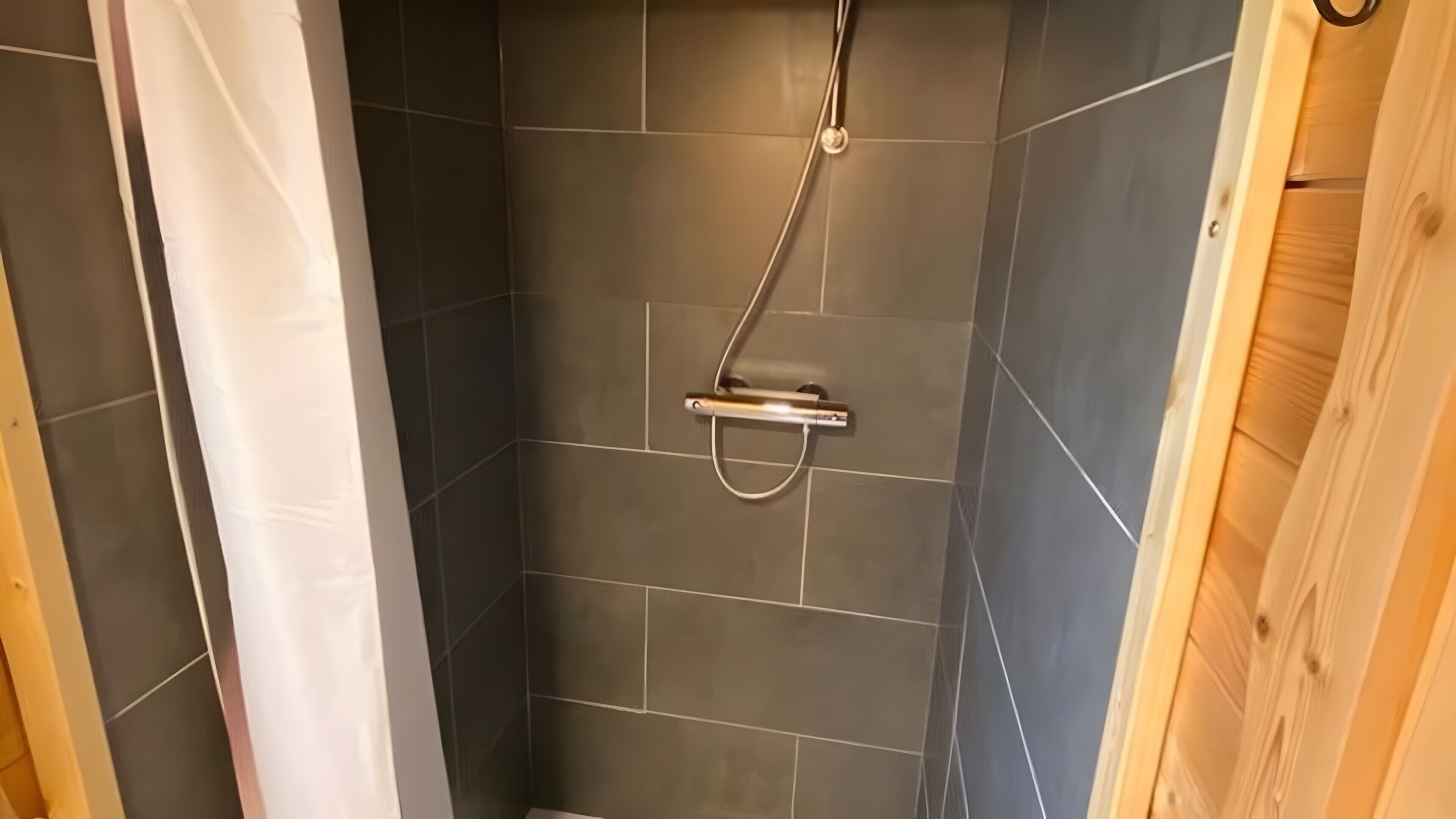 Een douche met een handdouche, betegelde wanden en houten lambrisering.