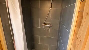 Een douche met een handdouche, betegelde wanden en houten lambrisering.