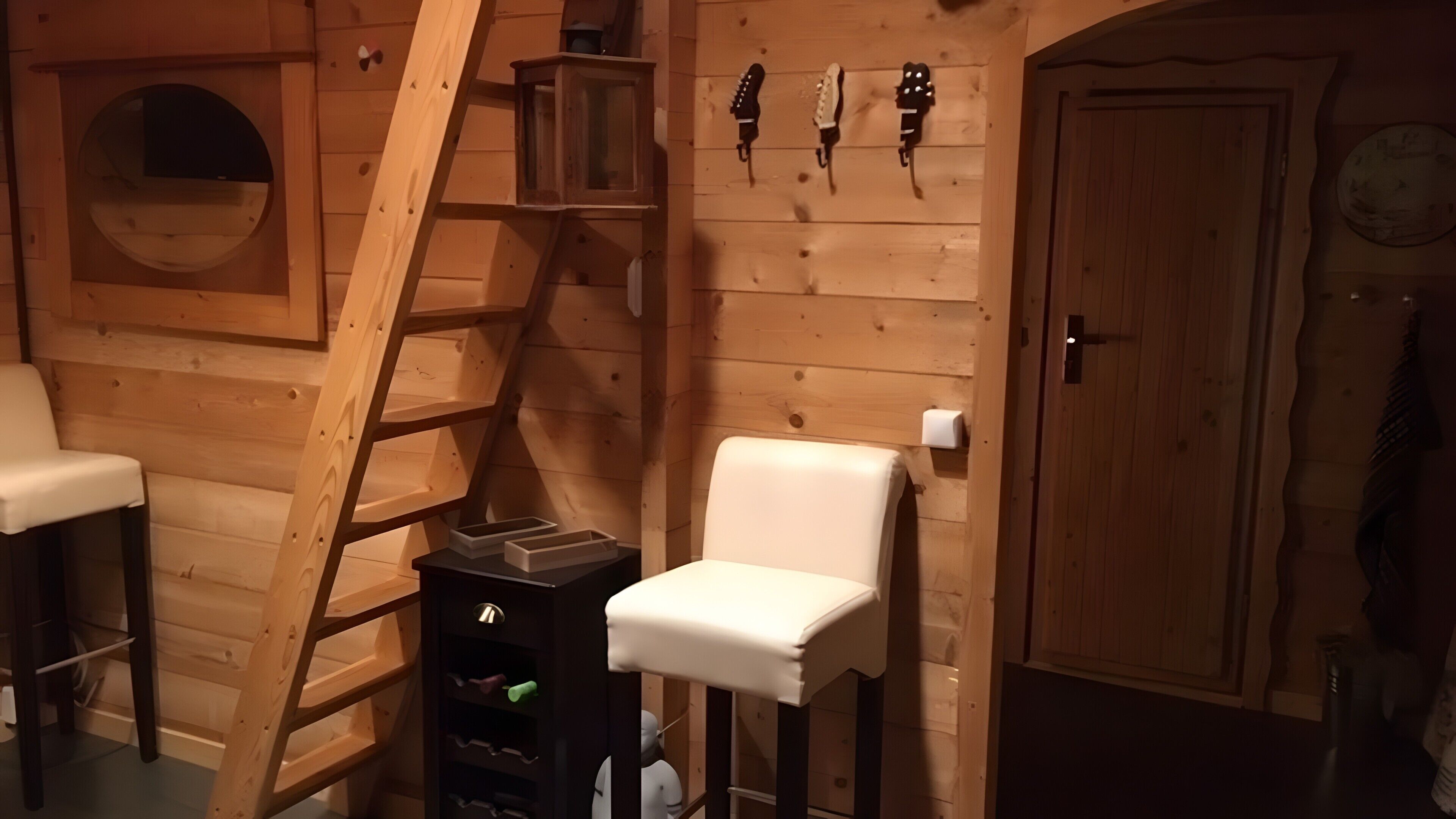 Un interior de madera con una escalera, una silla blanca, una puerta de madera y un pequeño estante con botellas.