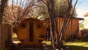 A wooden structure with a circular window and a door, surrounded by trees and a fence. - Holiday Home for 4 People (28 m²) in Coppenbrügge / Bäntorf (Coppenbrügge)
