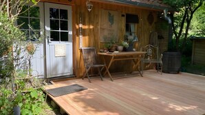 Un terrazzo in legno con tavolo e sedie, una porta e un muro con un cartello.