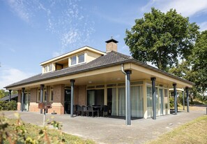 Een huis met twee verdiepingen, een overdekte patio, een schoorsteen en een gevel van baksteen.