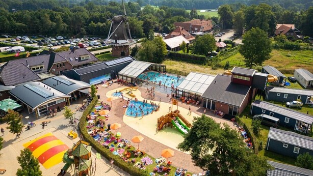 Een camping met een zwembad, een windmolen en een speeltuin.