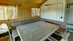 Een kamer met een grote houten tafel, zachte banken en een raam met gordijnen.