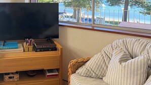Ein Zimmer mit Fernseher auf einem Holztisch, einem Korbstuhl und Meerblick durch ein Fenster.