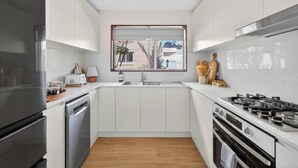 Eine moderne Küche mit weißen Schränken, einem Edelstahlkühlschrank, einem Gasherd und einem Fenster mit Außenblick.
